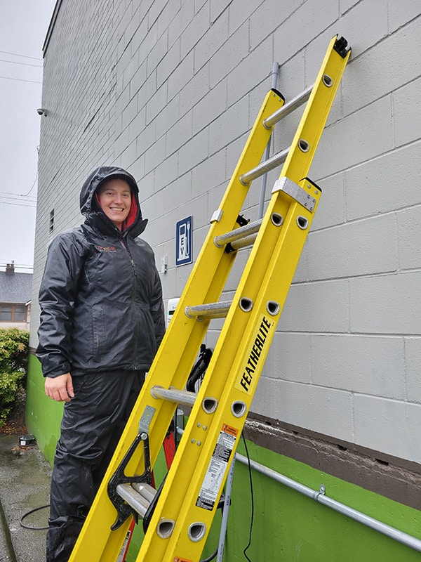 TCA Electric employee standing next to a ladder and a grey painted CMU Wall